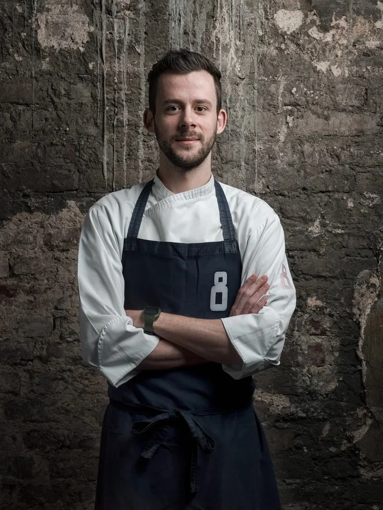 Portrait of a restaurant chef in an apron against a brick wall.